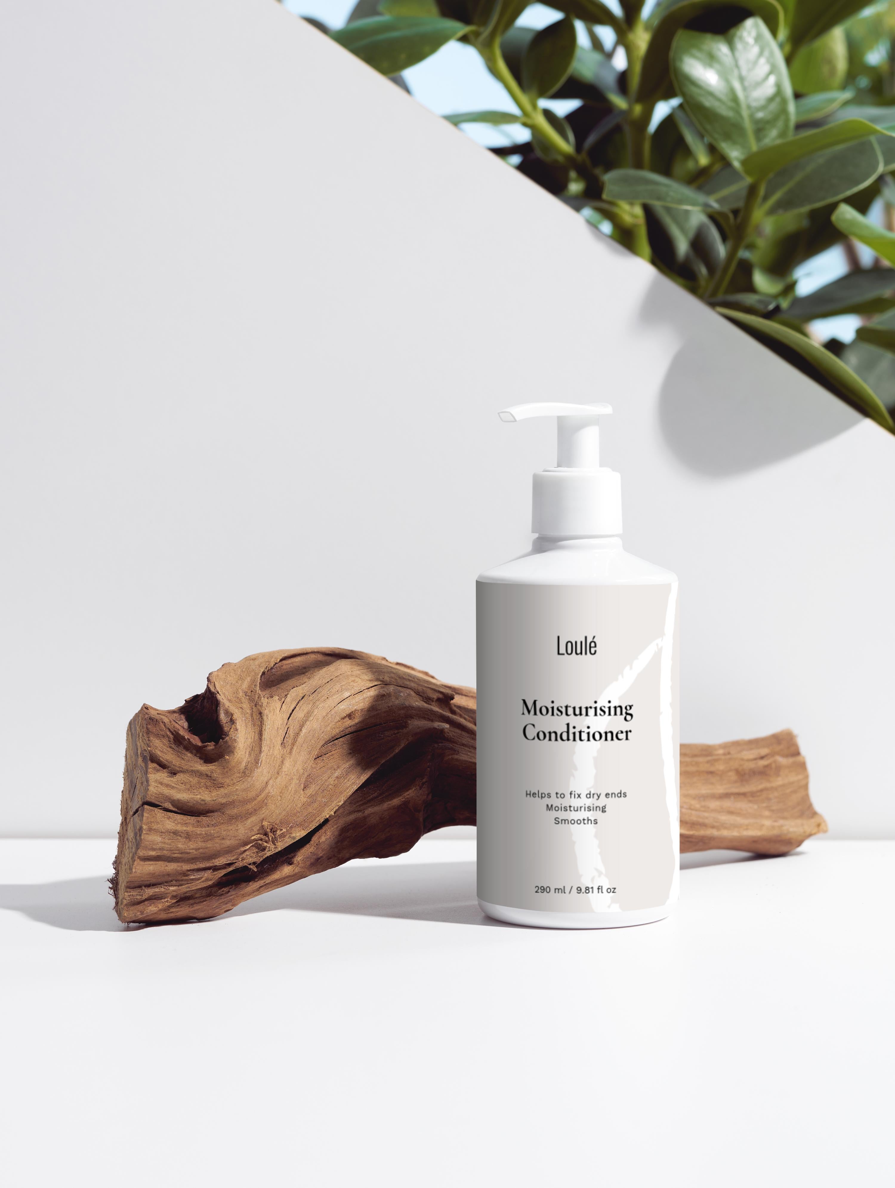 Loulé Moisturising Conditioner bottle with pump, placed on a natural wood piece, ideal for dry ends and smoothing hair. Features aloe juice and argan oil.