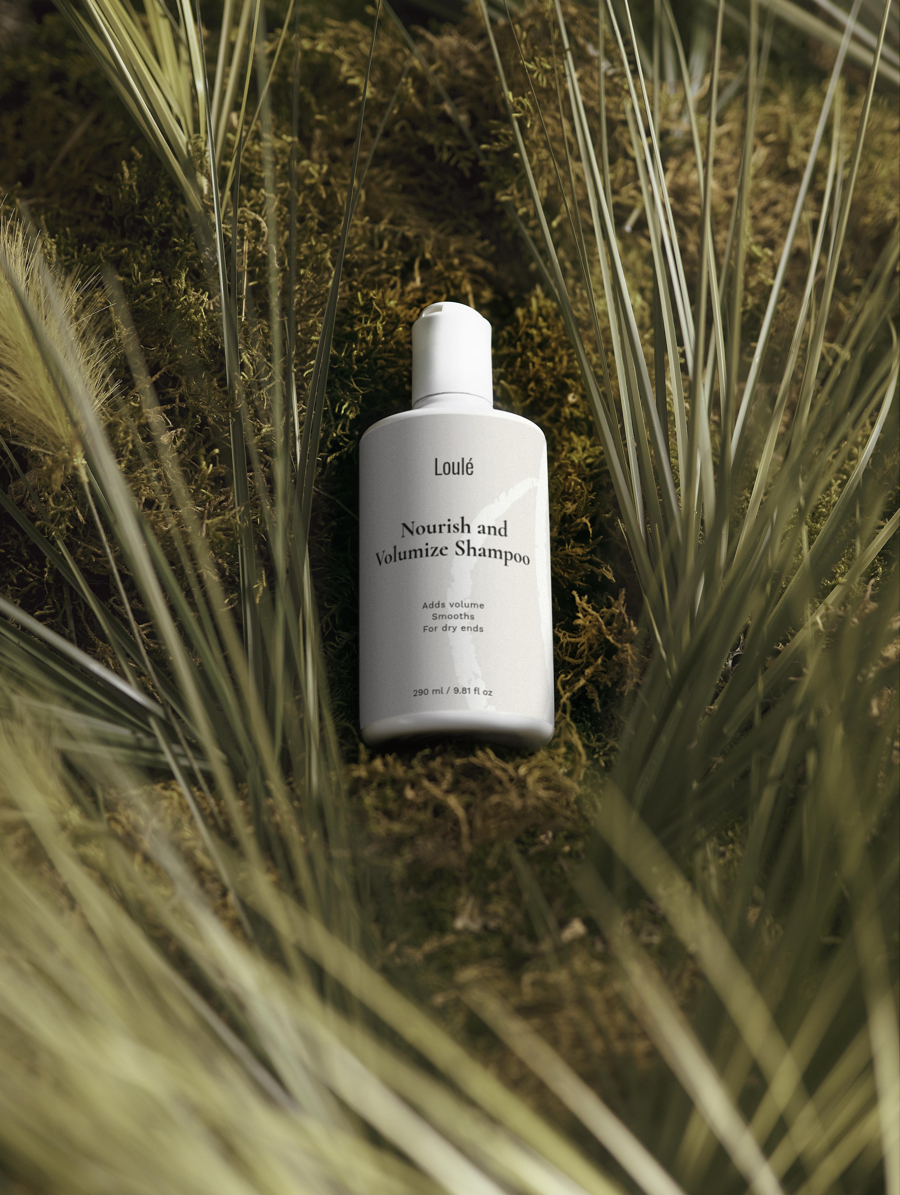 Loulé Skin Nourish and Volumize Shampoo in white bottle placed on natural moss and grass, ideal for dry ends and adding volume with wheat protein.
